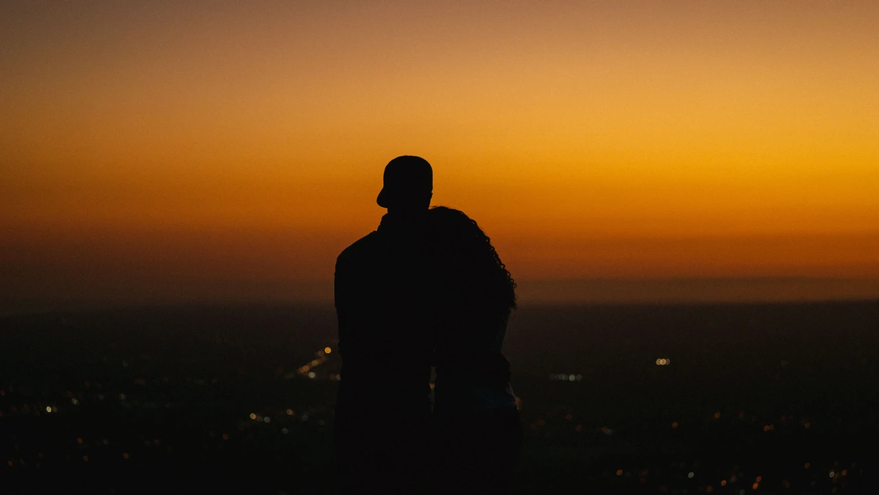 A couple in silhouette against a golden sunset over city lights