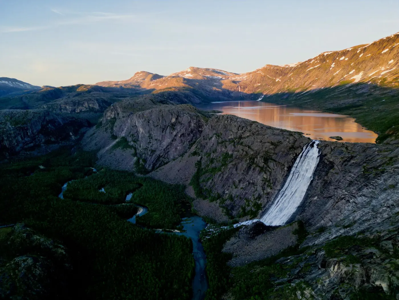 A waterfall and mountain lake at sunrise from the air