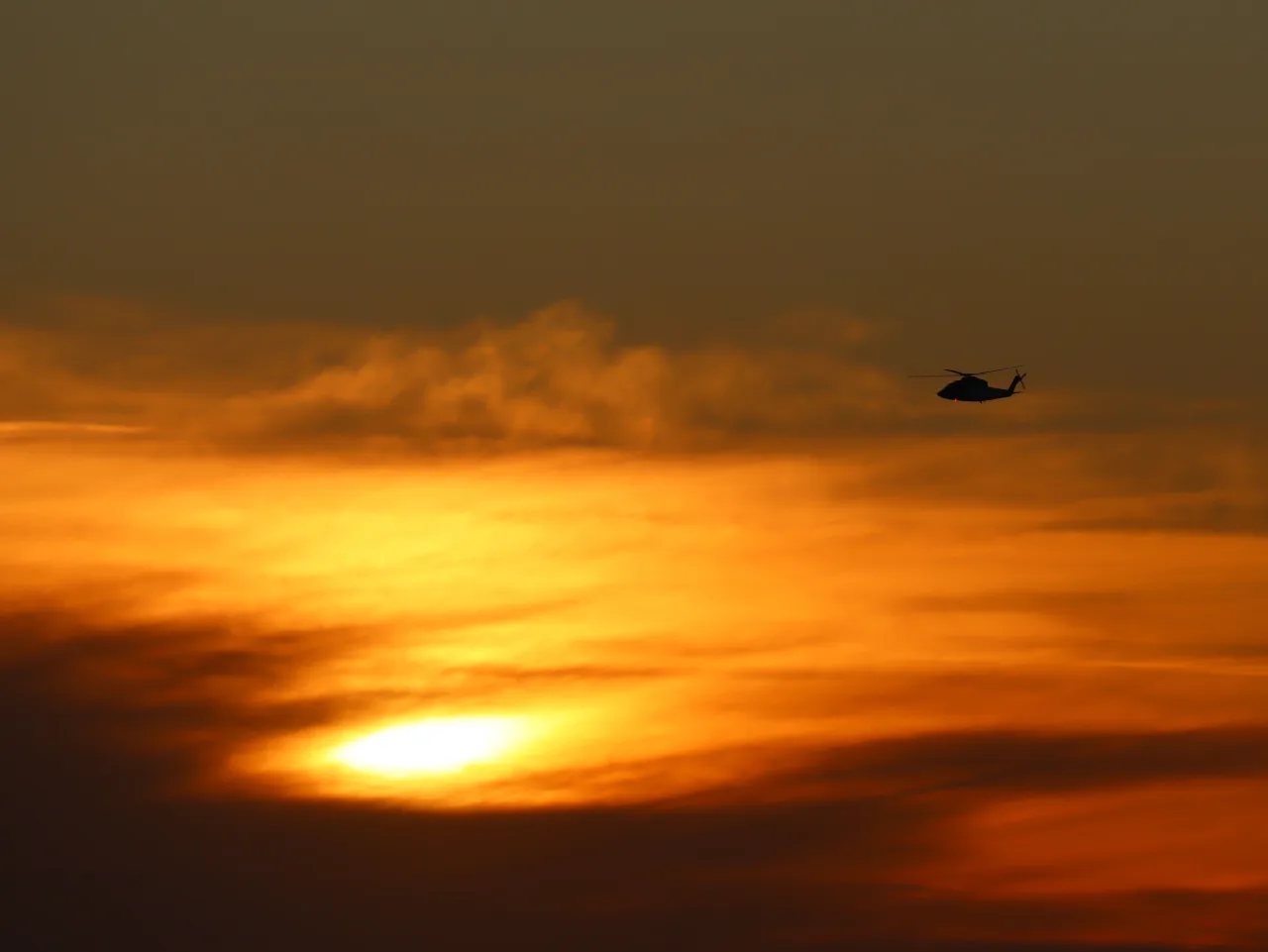 A helicopter in flight against a glowing sky
